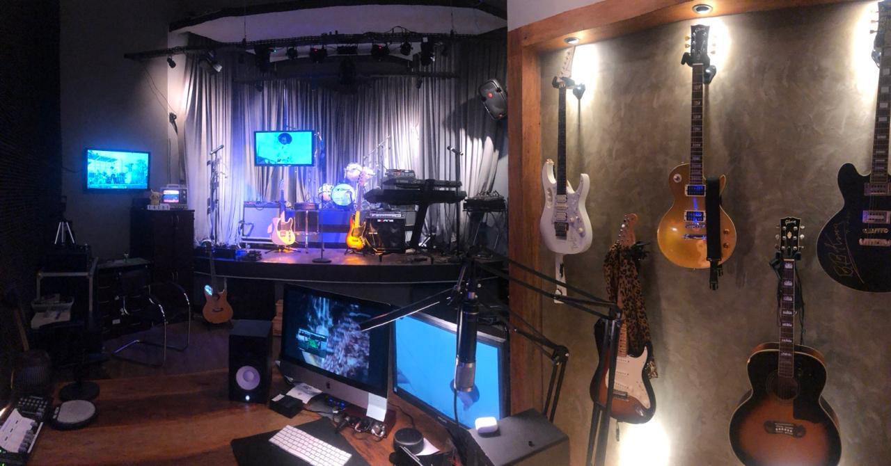 Estúdio com instrumentos musicais, área de trabalho e palco
